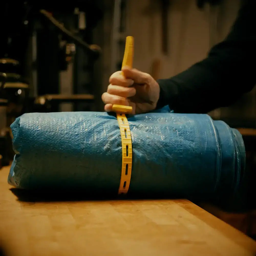 Hand securing blue industrial roll with yellow plastic strap in workshop