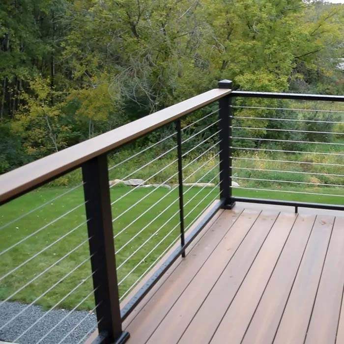 Modern deck railing with black posts and stainless steel cables, overlooking green yard and trees