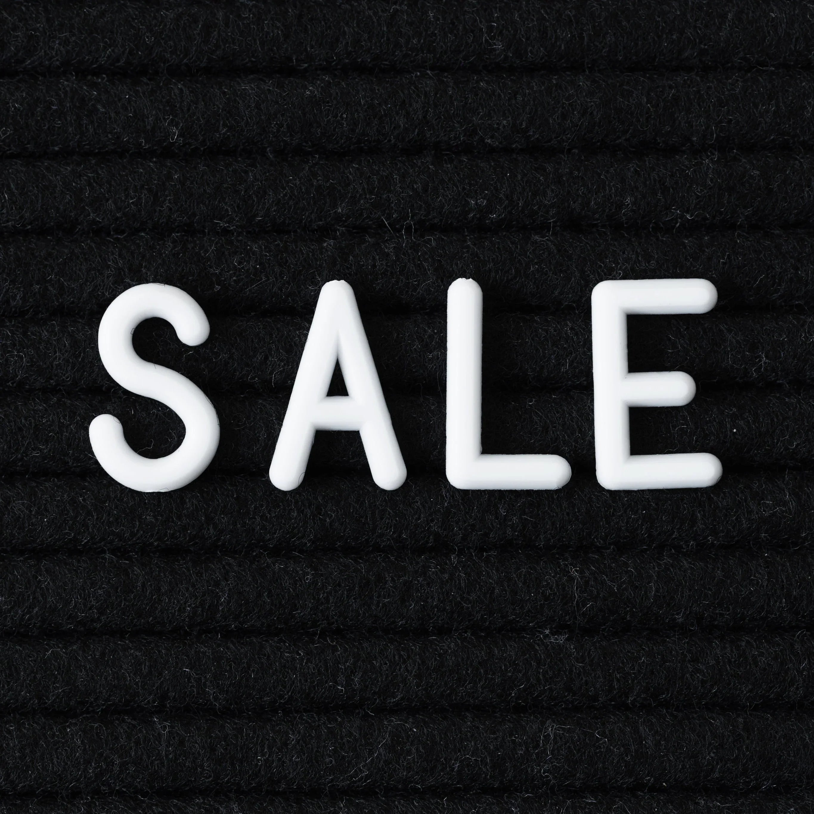 White plastic letters spelling SALE on textured black fabric background for promotion