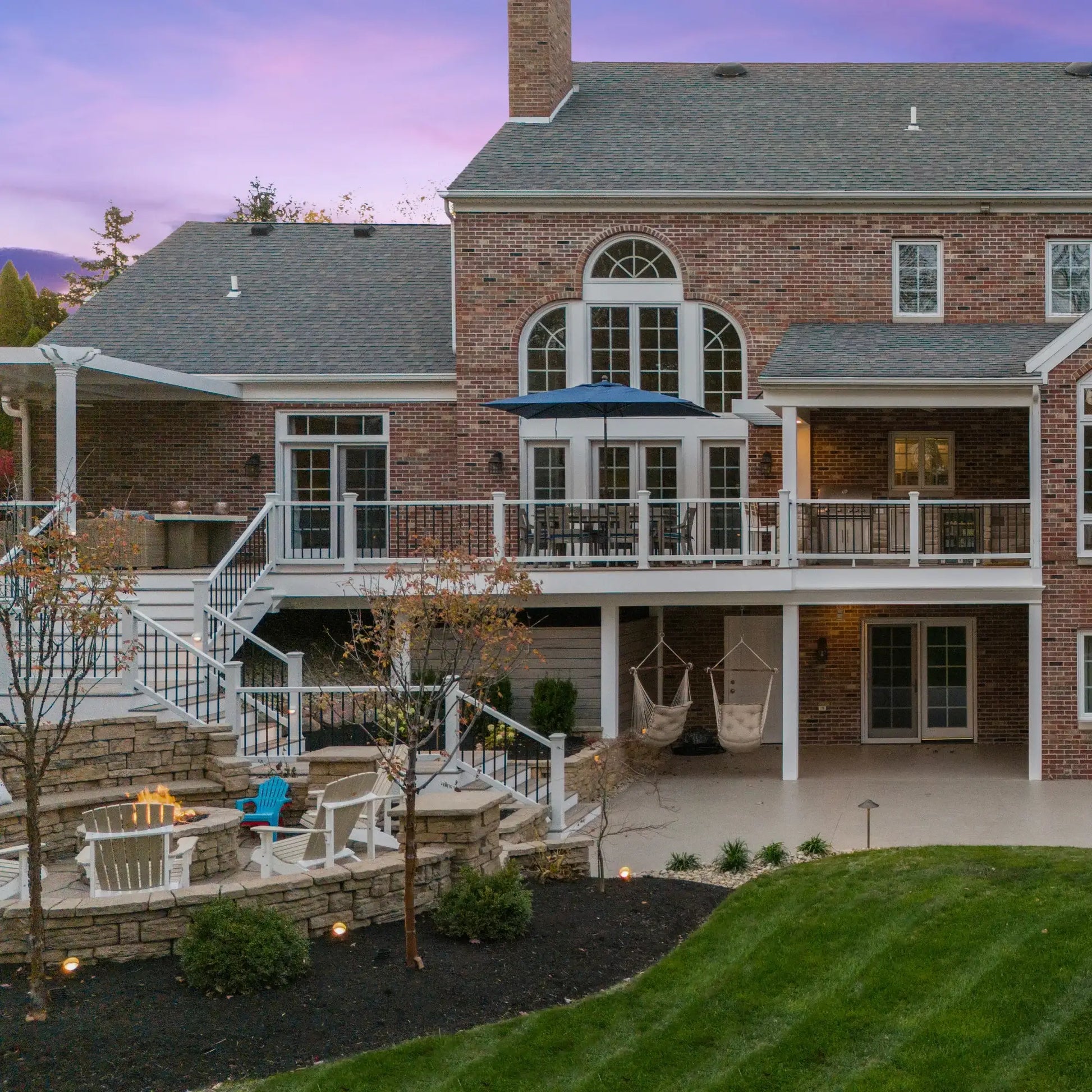 Luxury brick home with multi-level deck, fire pit, hammocks, and outdoor seating at dusk