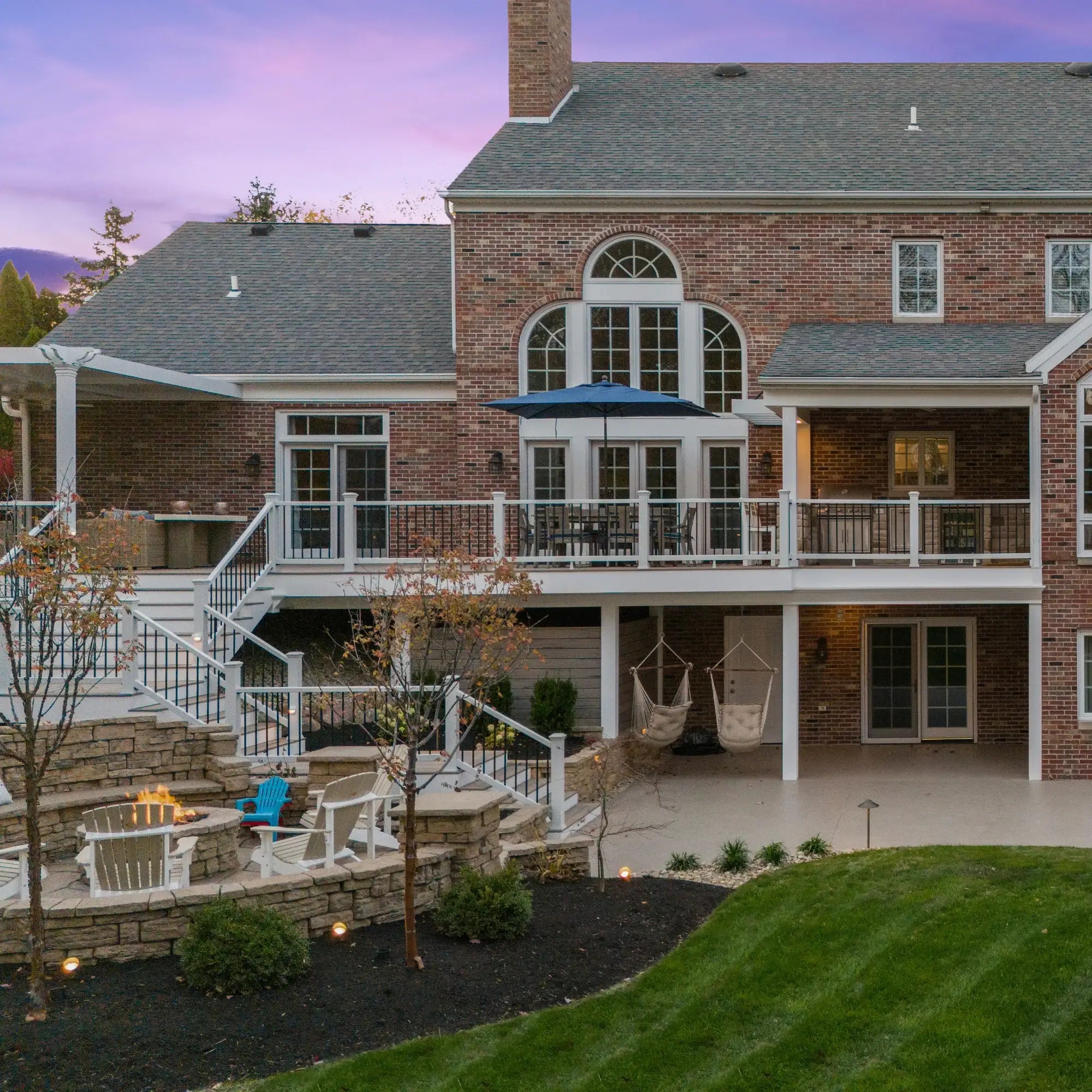 Luxury brick home with multi-level deck, fire pit, hammocks, and outdoor seating at dusk