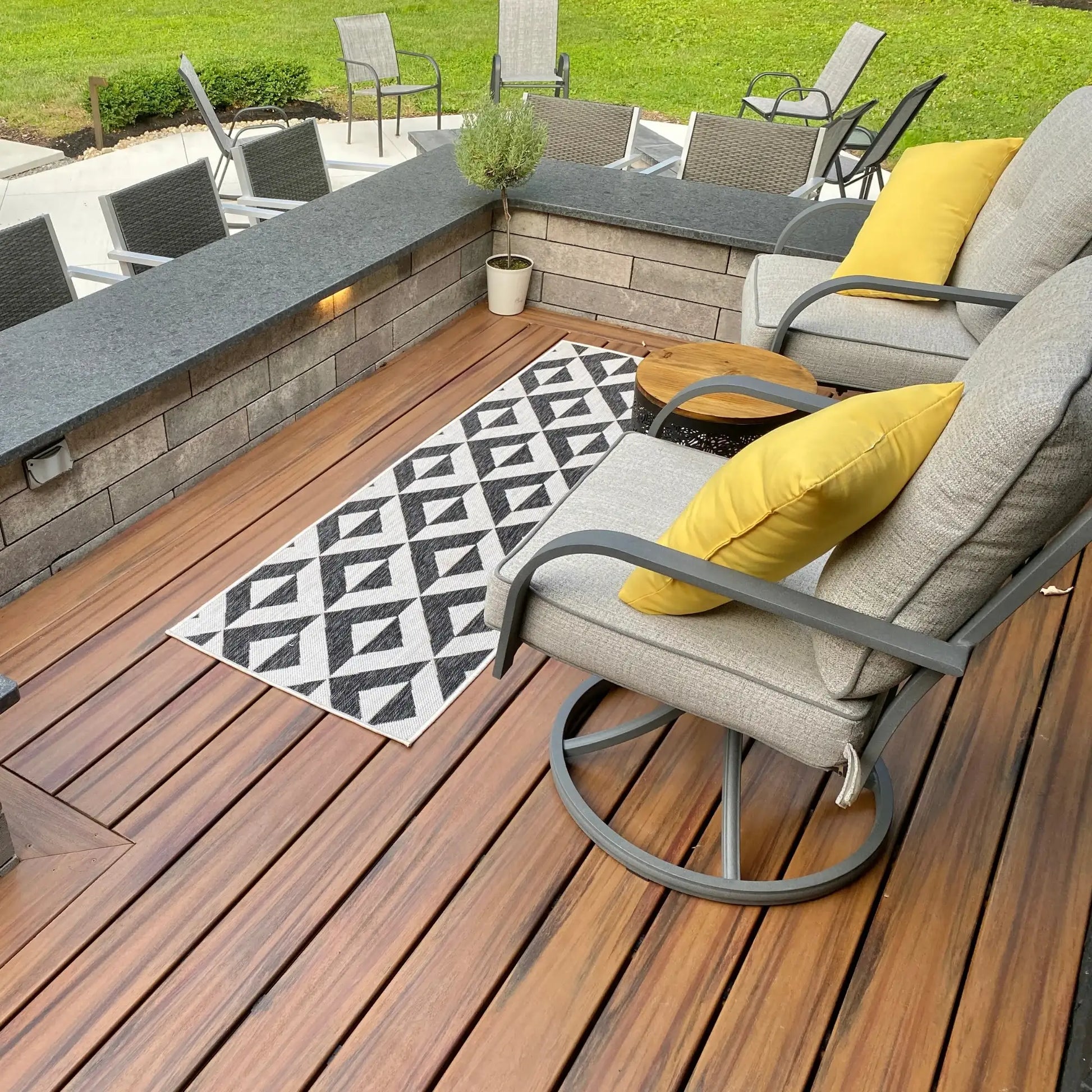 Modern outdoor deck with gray cushioned chairs, yellow pillows, and geometric rug