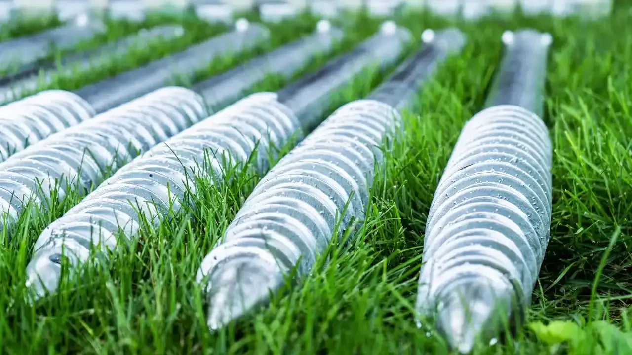 Metal ground anchors for industrial use, arranged on grass, ideal for securing equipment or structures.