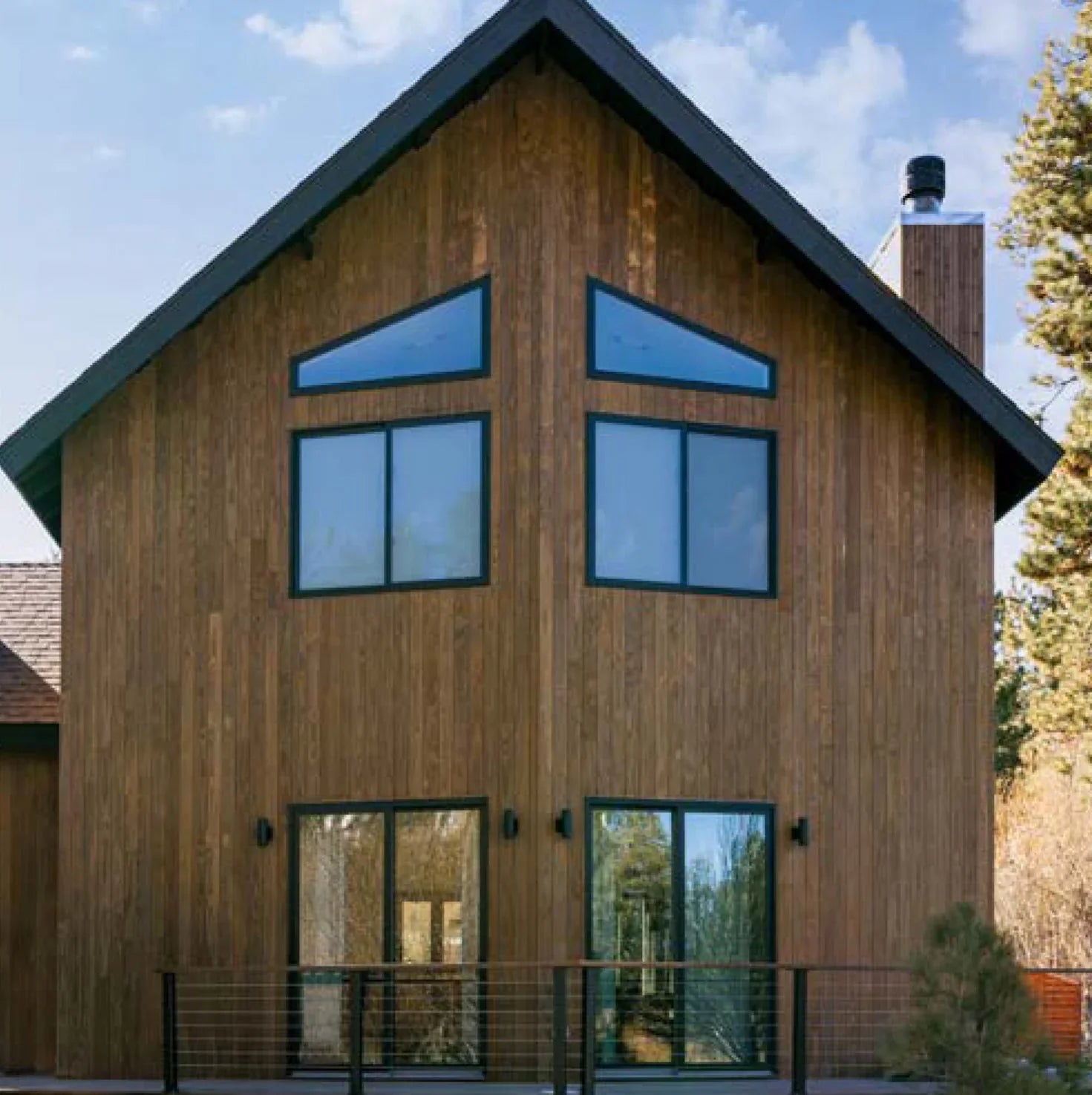 Modern house exterior with vertical wooden siding, large geometric windows, and black trim