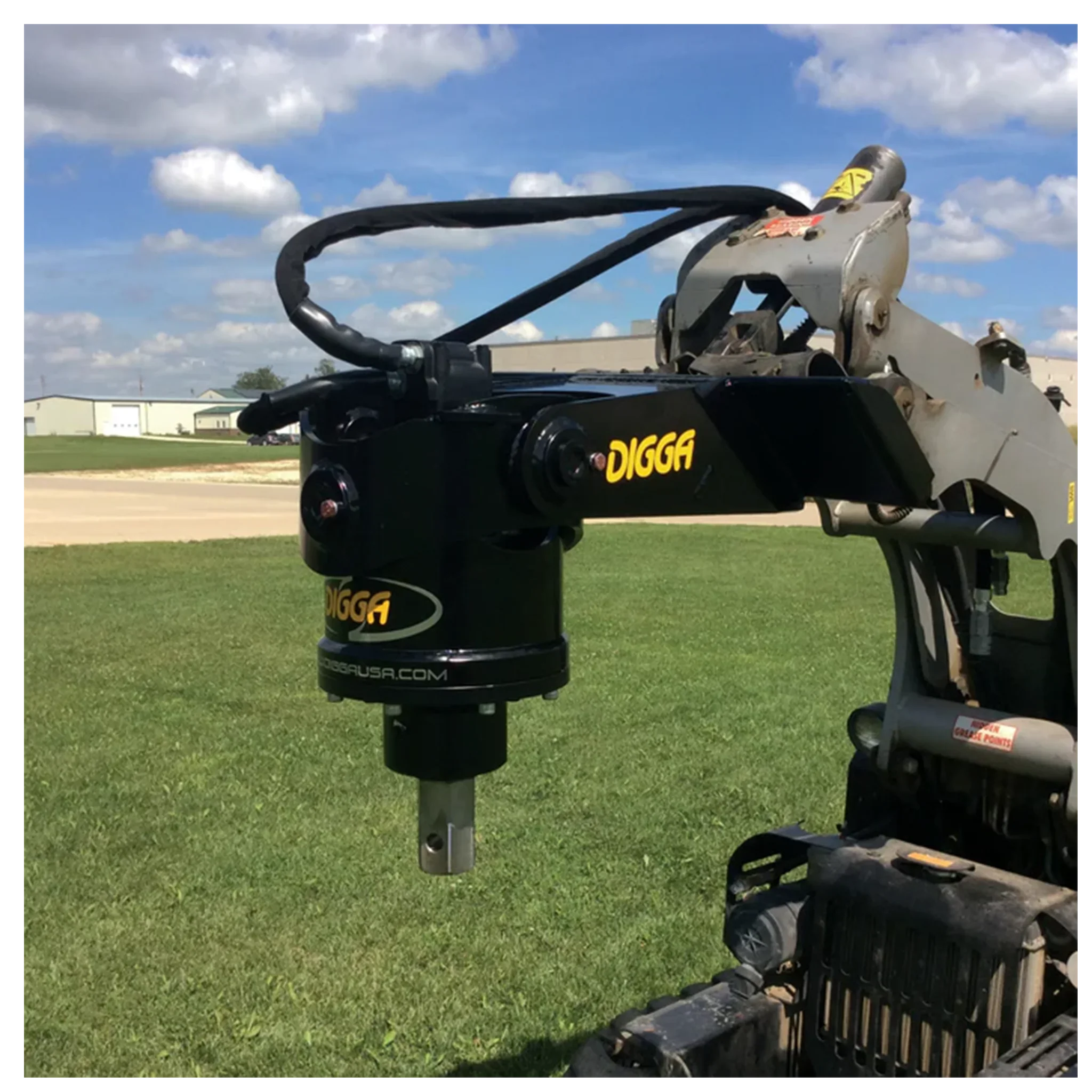 Digga mini skid steer auger drive attachment on construction equipment arm over grass field