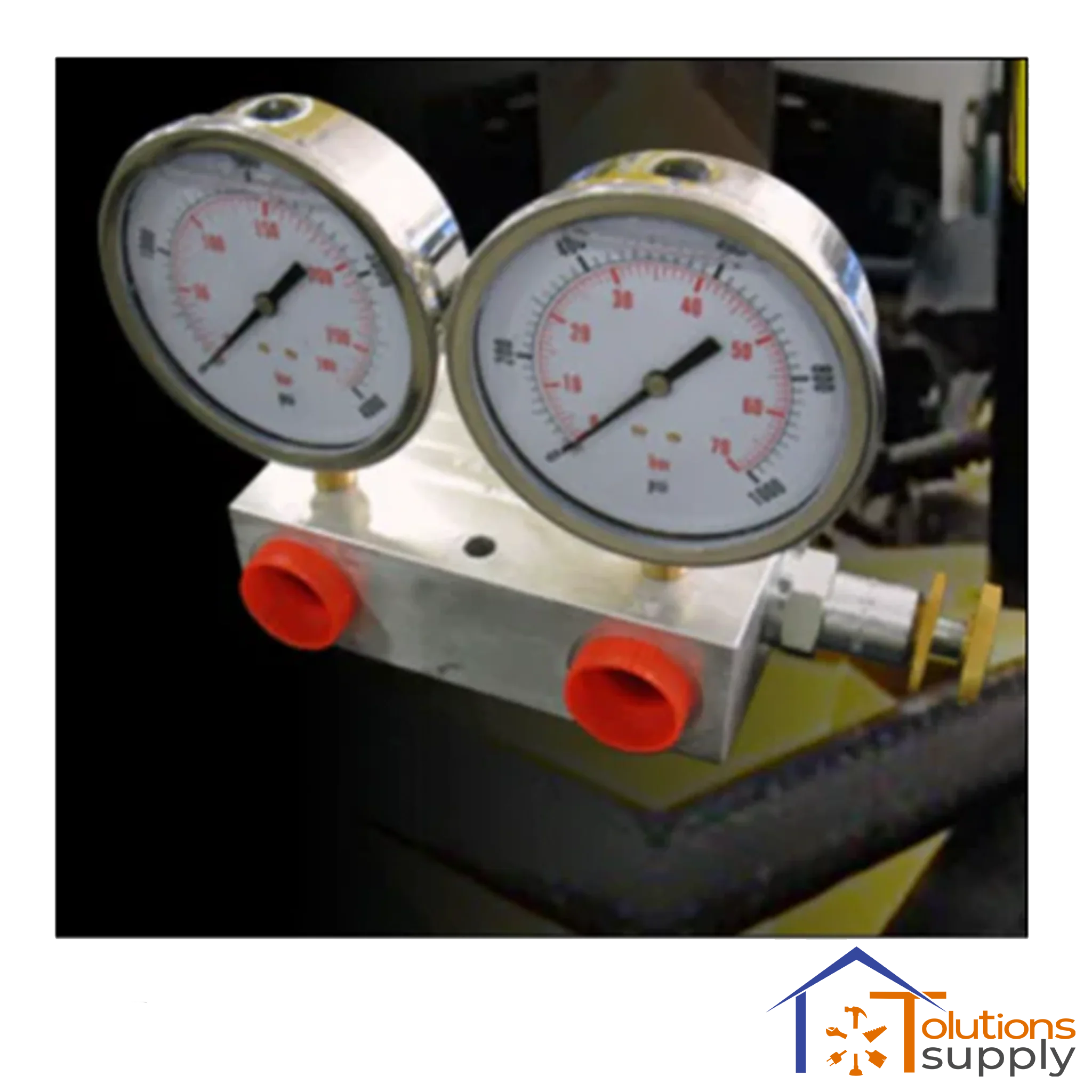 Close-up of dual metal pressure gauges with red connectors on industrial equipment