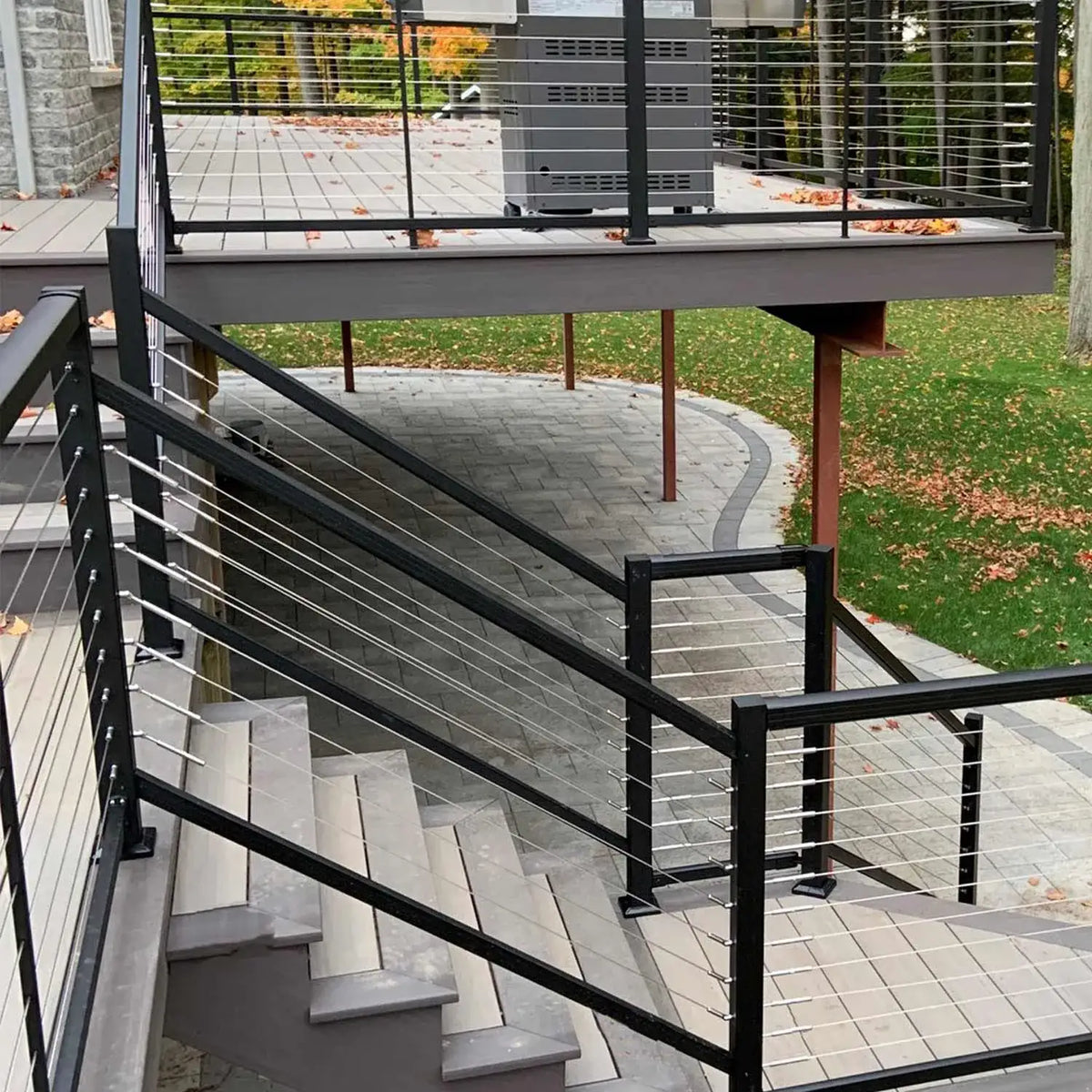 Modern black cable railing system on outdoor deck stairs with paver walkway and autumn leaves